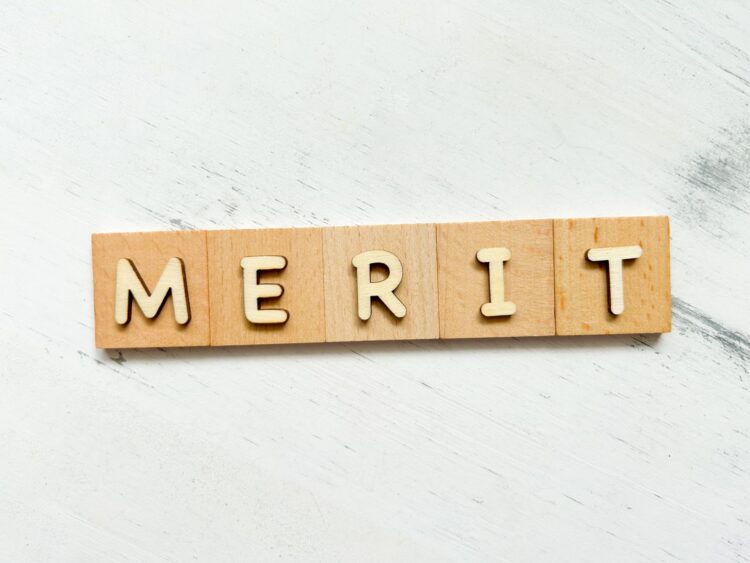 白い木目調の背景に、木製のタイルで作られた'MERIT'（メリット）という文字が並んでいる