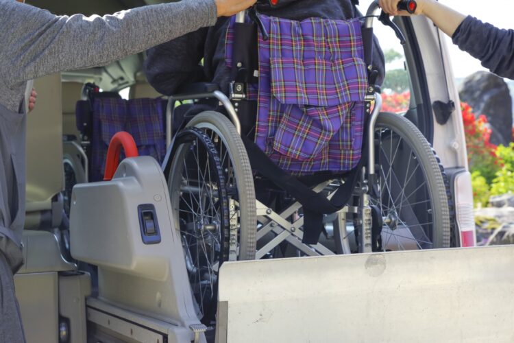 「車いすの高齢者を介護リフトで車に乗せる介助の様子。」