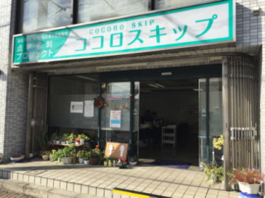 「『ココロスキップ』という看板が掲げられた建物の外観。入口前に植物が並べられている。 