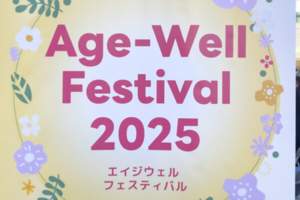 花のイラストに囲まれたデザインの看板に、大きく『Age-Well Festival 2025』と書かれ、その下に日本語で『エイジウェル フェスティバル』と表記されている。