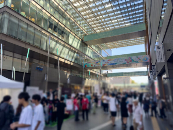 二子玉川ライズのガレリアで行われた Age-Well Festival 2025。天井の高いガラス張りの通りに、多くの来場者が集まり、色とりどりの横断幕が飾られている