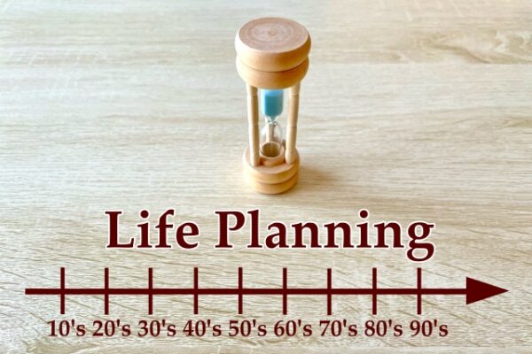 木製の砂時計がテーブルの上に置かれ、下部には「Life Planning」と書かれた文字と、10代から90代までを示す年代ごとの目盛り付きの横長の矢印が描かれている。