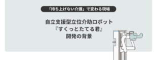 淡いグレーの背景の中央に、黒い文字で大きく「自立支援型立位介助ロボット『すくっとたてる君』開発の背景」と書かれている。 その上には黒い帯に白文字で「持ち上げない介護」で変わる現場、という見出しがある。 右側には白と水色を基調とした介助ロボットのイラストが描かれ、立ち上がりをサポートする形状が示されている。 全体として、介護の負担軽減や自立支援をテーマにしたスライドのタイトル画像。