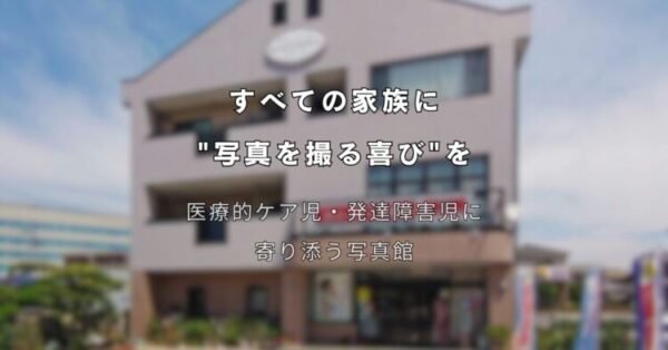 3階建ての建物を背景に、中央に白い文字でキャッチコピーが書かれている。 上部の文字は「すべての家族に “写真を撮る喜び”を」。 その下には「医療的ケア児・発達障害児に寄り添う写真館」と書かれている。 建物の外観は淡いベージュ色で、正面に大きな窓と看板があり、晴れた青空の下で撮影されている。 障害や医療ケアが必要な子どもたちと家族に、写真撮影の楽しさを届ける想いを表現したメインビジュアル。