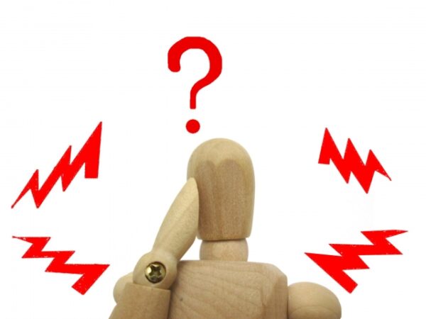 木製の人形が頭に手を当て、赤いハテナマークと稲妻に囲まれている。 困惑や戸惑いを表すような様子がユーモラスに描かれている。