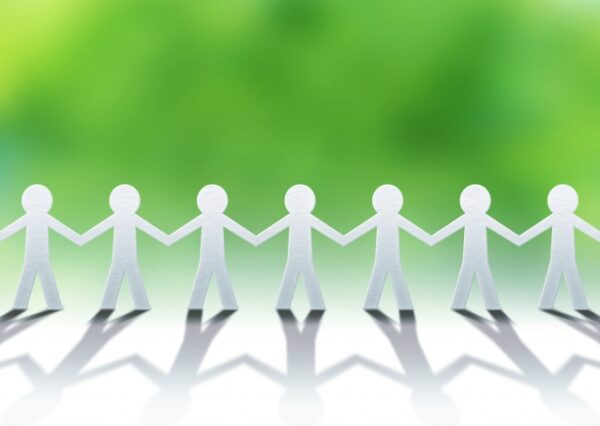 緑の背景の前で、紙で作られた人型が手をつなぎ並んでいる。 つながりや支え合いを象徴する、やさしく穏やかなイメージ。