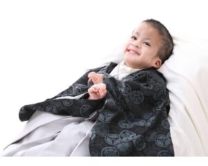 黒の紋付き袴を着た男の子が、白い布の上でやさしく微笑んでいる。 柔らかな表情から、穏やかな時間と温かい心の通い合いが伝わる。