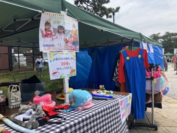 屋外イベントのテントに、子ども向けのコスプレ体験コーナーが並んでいる。 衣装や小道具が整えられ、楽しそうな雰囲気が伝わってくる。