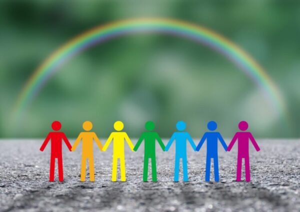 虹の下で、色とりどりの人型が手をつなぎ、横一列に並んでいる。 多様な人々が共に生き、支え合う姿をやさしく表している。