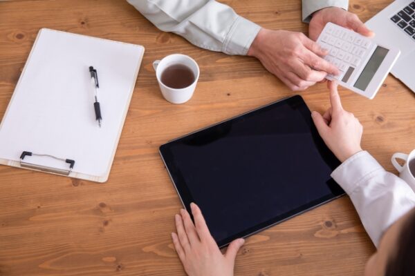 机の上でタブレットを前に、電卓を使いながら二人で数字を確認している様子。 落ち着いた空間の中で、丁寧に相談しながら進めている時間が感じられる。