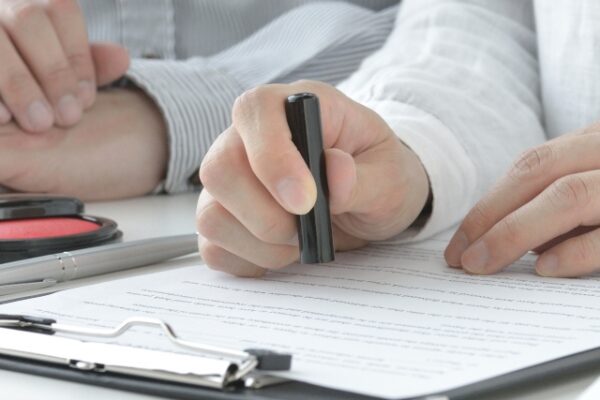 書類に向かい、印鑑を手にして丁寧に押そうとしている手元の様子。 大切な手続きを進める、静かで確かな一場面。