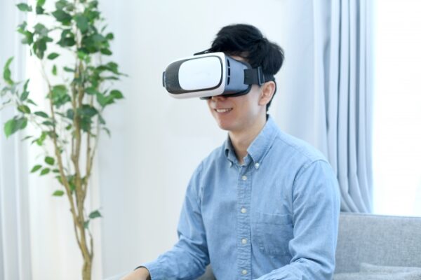 VRゴーグルを装着した男性が、明るい室内のソファに座り、笑顔でVR体験をしている様子。